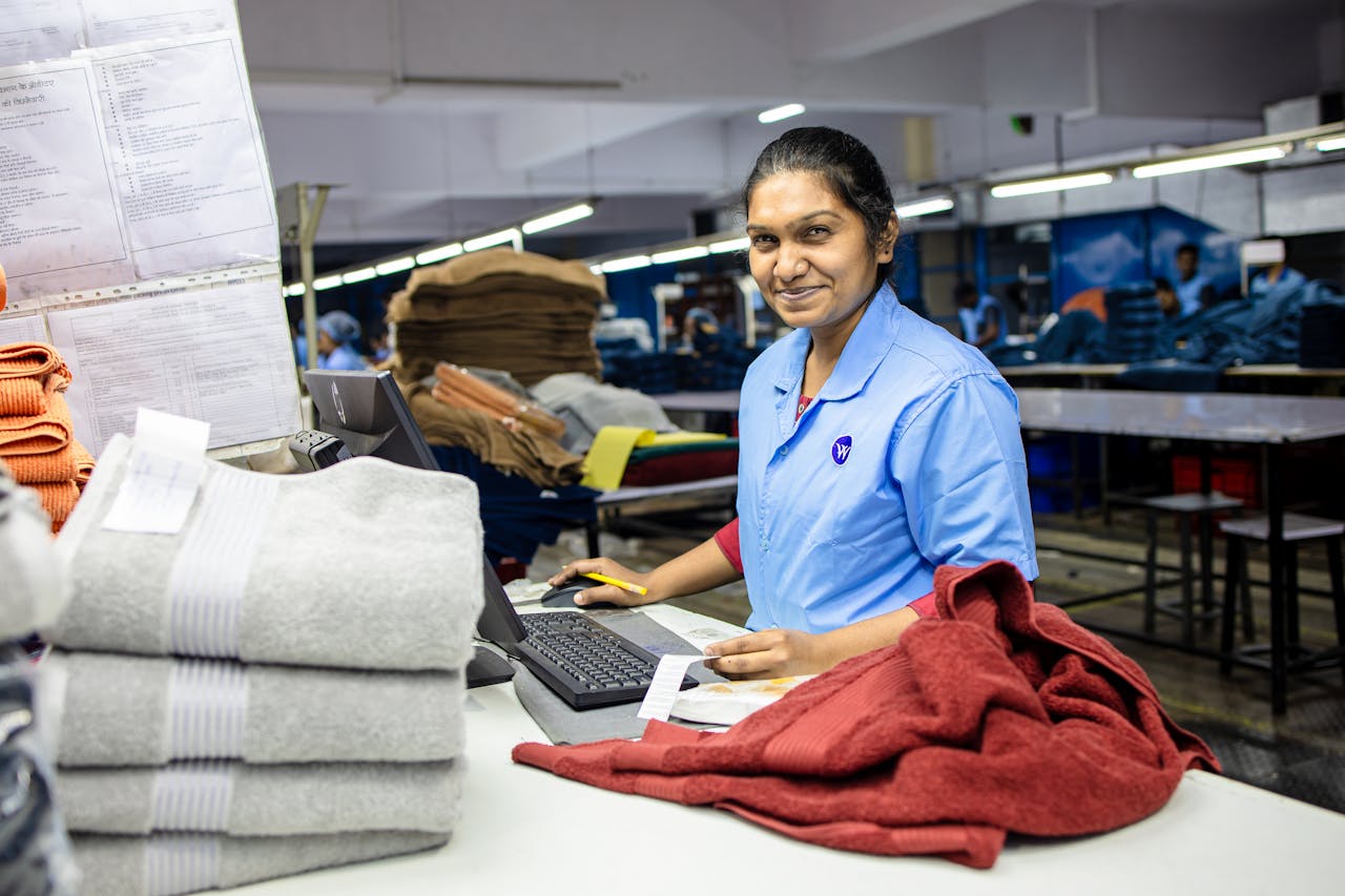 A factory worker in a textile manufacturing plant with folded fabrics nearby, exuding confidence and professionalism.